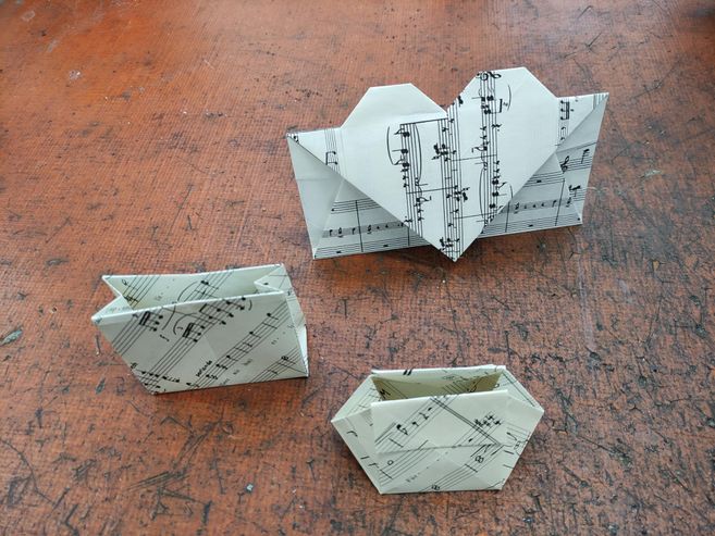 3 gefaltete Objekte aus Notenpapier. Zwei Taschen und ein Briefumschlag mit einem gefaltetem Herz.
