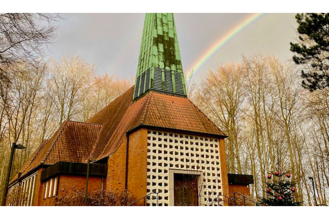 Kirche mit grünem Turm und Regenbogen im Hintergrund.
