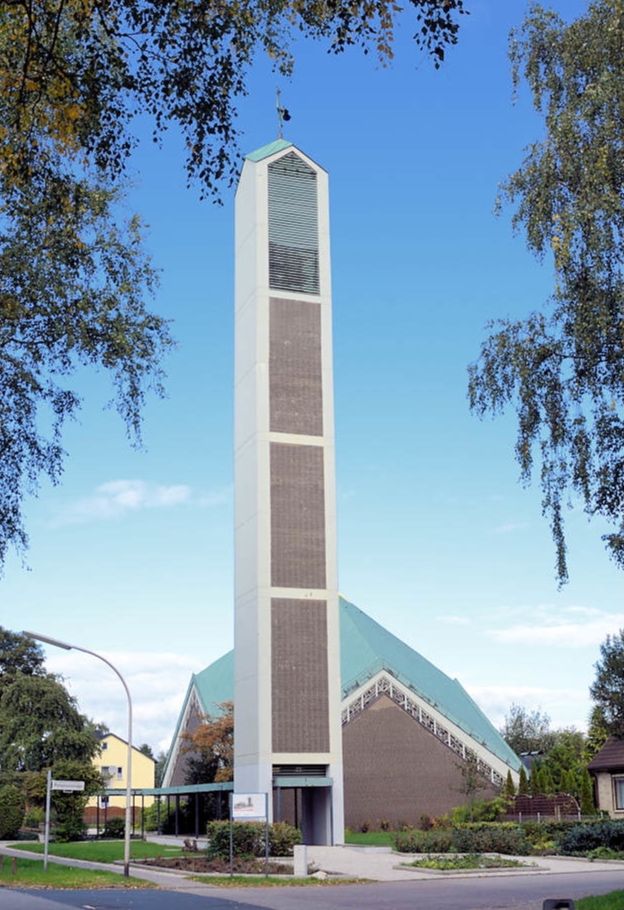 Moderne Kirche mit hohem Turm und grünem Dach, umgeben von Bäumen und einem blauen Himmel.