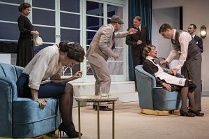 Theaterszene mit mehreren Personen in einem Wohnzimmer.