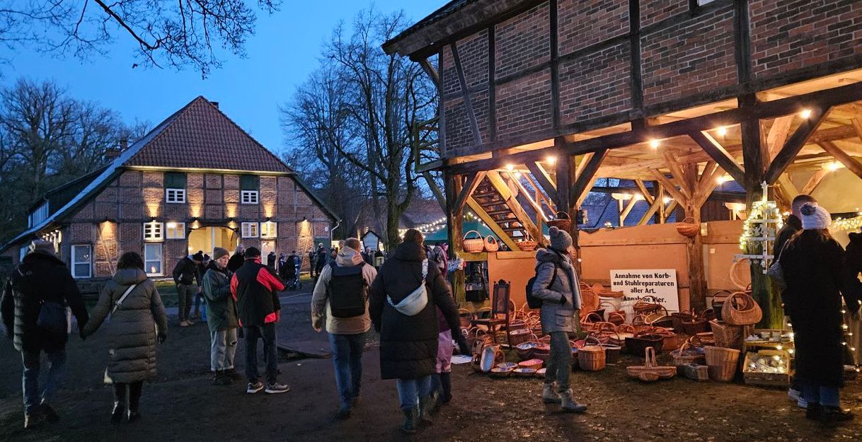 Man sieht den Weihnachtsmarkt auf dem Gut Rehrhof mit Fachwerkgebäuden, Kunsthandwerkern und Lichtern.