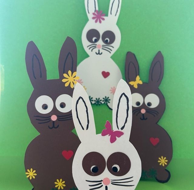 Vier aus Papier gebastelte Hasen vor einem grünen Hintergrund.