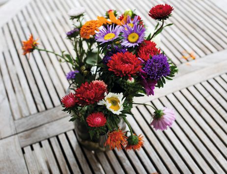 Ein bunter Blumenstrauß in einer Vase auf einem Holztisch mit Gittermuster.