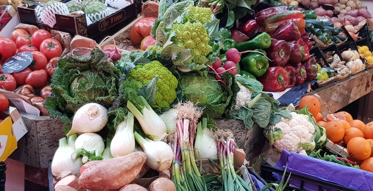 Ein Marktstand mit frischem Obst und Gemüse, darunter Tomaten, Paprika, Fenchel, Blumenkohl und Süßkartoffeln.