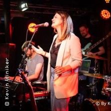 Frau singt auf einer Bühne mit Band im Hintergrund.