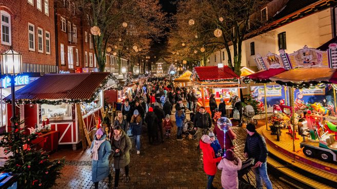 Menschenmenge auf dem Stader Weihnachtsmarkt mit beleuchteten Ständen und Karussell.