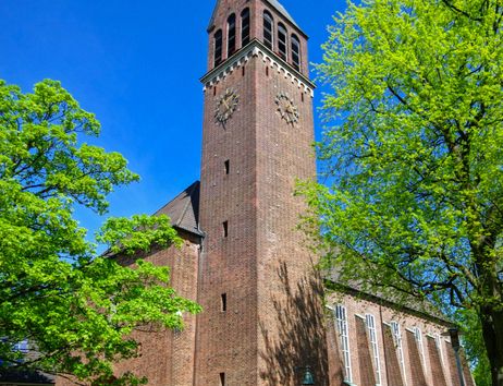 Backsteinkirche mit Turm und grünen Bäumen im Vordergrund.