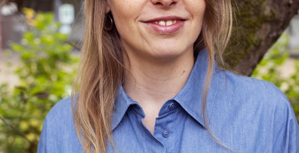 Eine junge Frau mit langen blonden Haaren und einer blauen Bluse lächelt in die Kamera