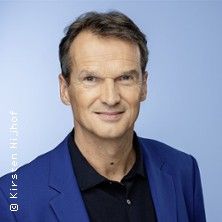 Porträt eines Mannes in einem blauen Anzug vor einem hellblauen Hintergrund.