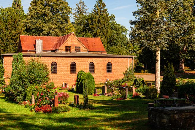 Eine Kapelle aus roten Ziegelsteinen auf einem alten Friedhof, umgeben von Bäumen und Grabsteinen.