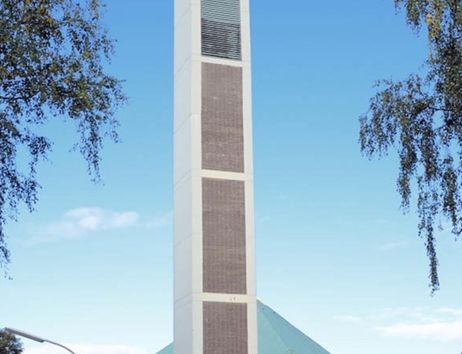 Moderne Kirche mit hohem Turm und spitzem Dach, umgeben von Bäumen.