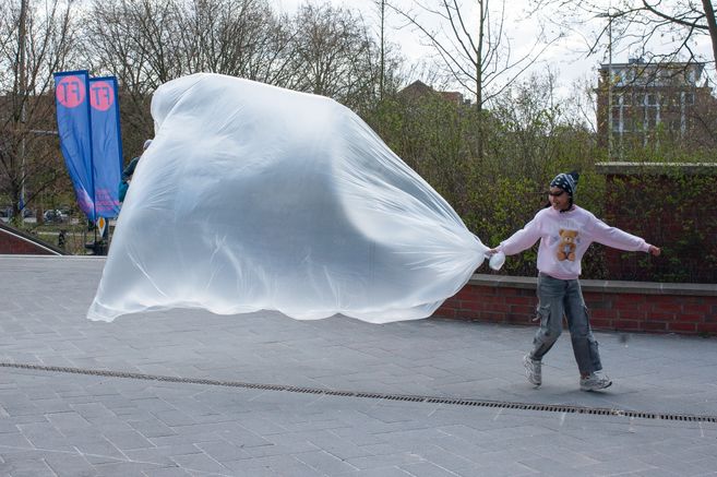 A girl is dragging a huge, thin plastic bubble behind her, filled with a large amount of air.