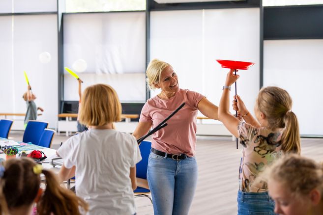 Eine Frau zeigt Kindern, wie man Teller auf Stöcken balanciert.