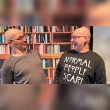 Zwei lachende Männer vor einem Bücherregal.