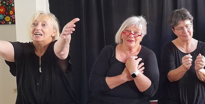 Drei Frauen in schwarzer Kleidung führen eine Improvisationstheater-Szene auf.