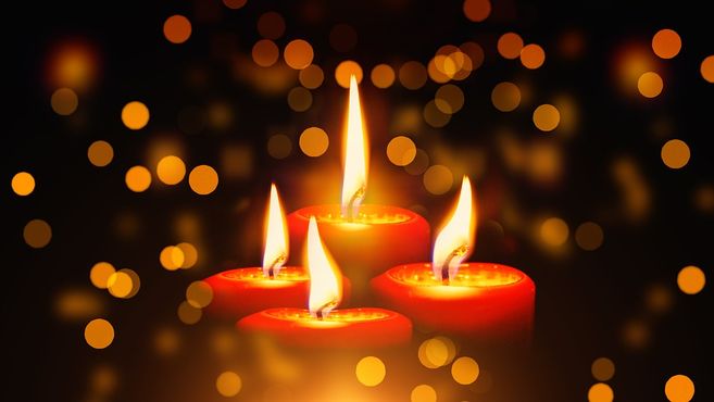 Vier brennende Adventskerzen mit unscharfen Lichtern im Hintergrund.