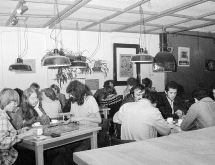 Schwarz-Weiß-Foto von Menschen, die in einem Café an Tischen sitzen und sich unterhalten.