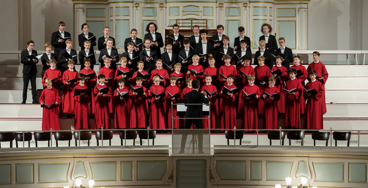 Ein Knabenchor in roten Roben singt auf einer Bühne vor einer Orgel.