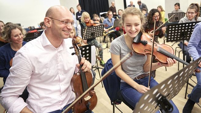 Menschen spielen gemeinsam Geige in einem Orchester.