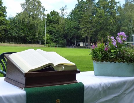 Ein Altar mit einer offenen Bibel und Blumenschmuck auf einem Tisch, der auf einem Fußballfeld steht.