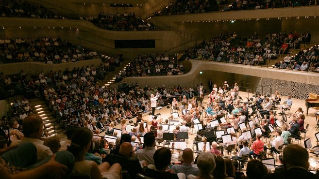 Ein Orchester spielt in einem voll besetzten Konzertsaal der Elbphilharmonie.
