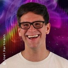 Ein lächelnder Mann mit Brille vor einem bunten, psychedelischen Hintergrund.