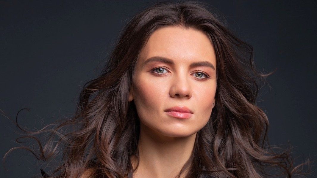 Porträt einer Frau mit langen, dunklen Haaren vor einem dunklen Hintergrund.