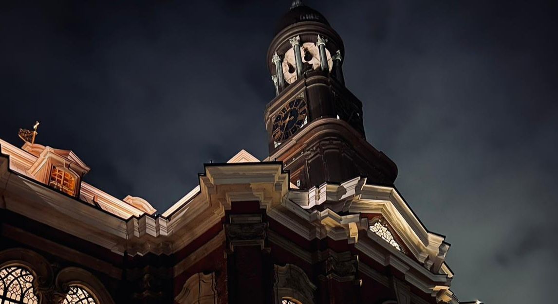 Nachtaufnahme der St. Michaelis Kirche mit beleuchtetem Turm und dunklem Himmel.