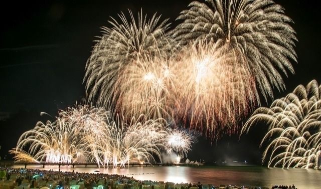 Ein großes Feuerwerk erleuchtet den Nachthimmel über einem Strand an der Ostsee, während Menschen am Ufer zuschauen.