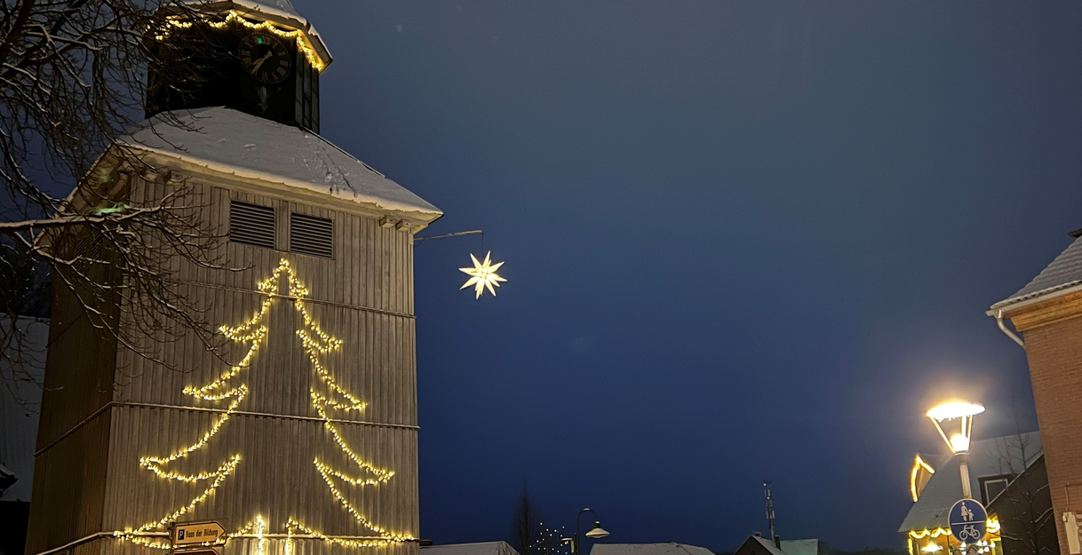 Beleuchteter Kirchturm und Straße in Visselhövede bei Nacht, geschmückt mit Weihnachtslichtern und Schnee.