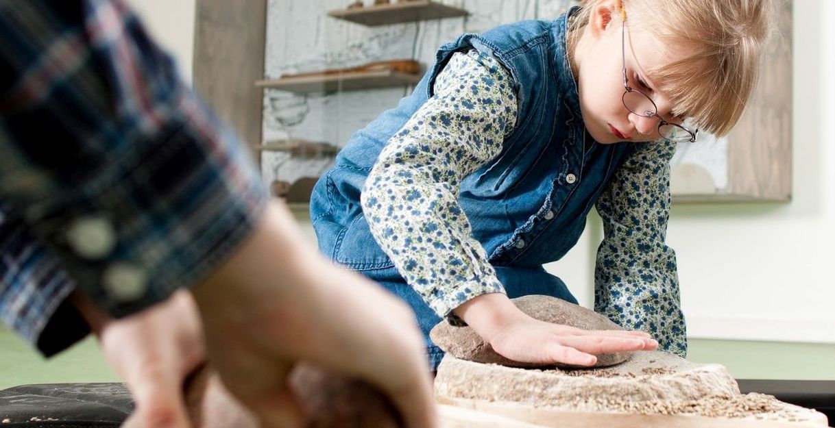 Ein Kind schleift mit einem Stein auf einer Holzoberfläche in einem Museum.