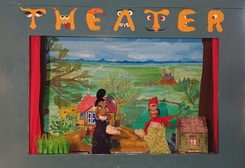 Puppentheaterbühne mit zwei Puppen vor Landschaftskulisse.