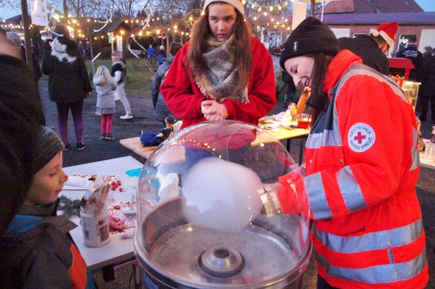 Person in roter Jacke macht Zuckerwatte auf einem Weihnachtsmarkt.