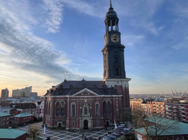 Die Kirche St. Michaelis in Hamburg mit ihrem markanten Turm und der Elbphilharmonie im Hintergrund bei Sonnenuntergang.