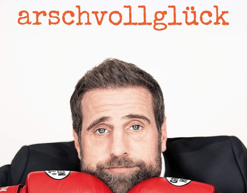 Ein Mann mit Bart und roten Boxhandschuhen stützt sein Kinn auf den Fäusten. Oben steht der Text 'Stefan Schöttler - arschvollglück'.