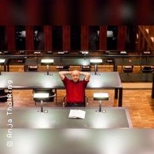 Eine Person sitzt entspannt an einem Tisch in einem Lesesaal.