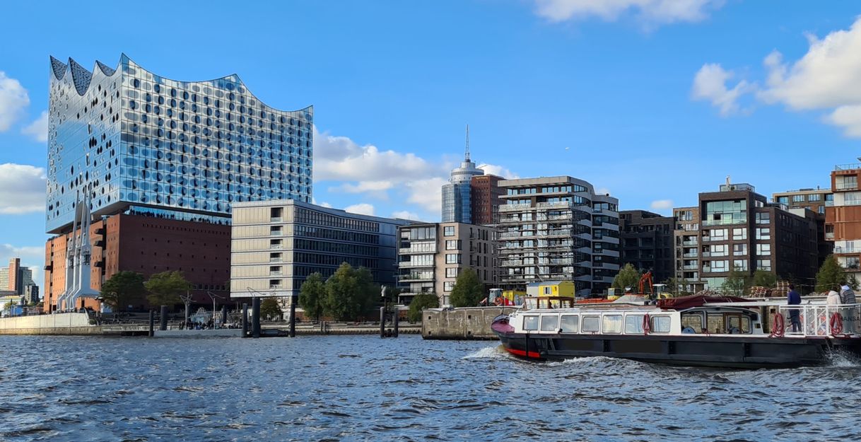 Eine Barkasse fährt auf der Elbe in Richtung der Elbphilharmonie, im Hintergrund stehen viele moderne Gebäude der HafenCity-Skyline