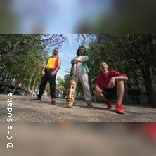 Drei Personen posieren im Freien mit einer bemalten Holzfigur.