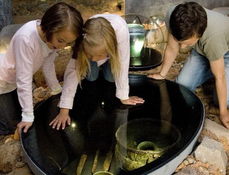 Drei Kinder betrachten Grabbeigaben in einem Museum.