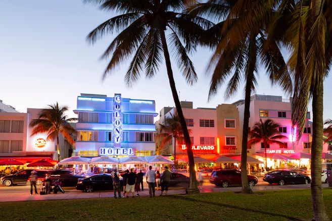 Das Bild zeigt den Ocean Drive in Southbeach Miami im Abendlicht mit leuchtenden Neon-Schildern. 