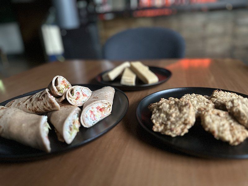 Drei Teller mit verschiedenen Speisen auf einem Holztisch: Wraps, Kekse und Riegel.