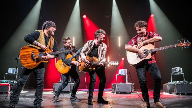 Vier Musiker spielen Gitarren auf einer Bühne mit roter Beleuchtung.