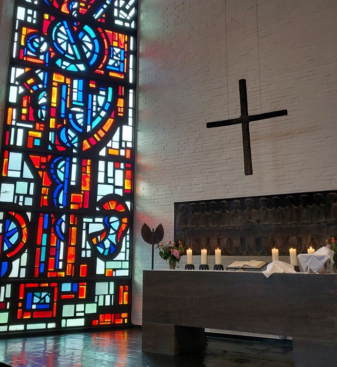 Altar der St. Johanneskirche mit Kerzen und Abendmahlsgedeck vor einem bunten Glasfenster.