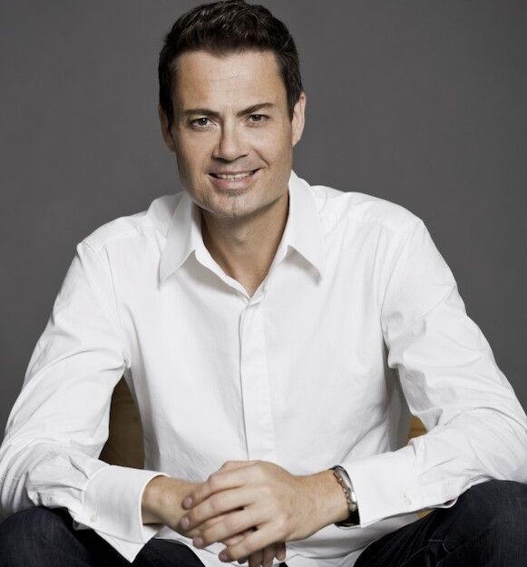 Mann in weißem Hemd sitzt und lächelt in die Kamera.