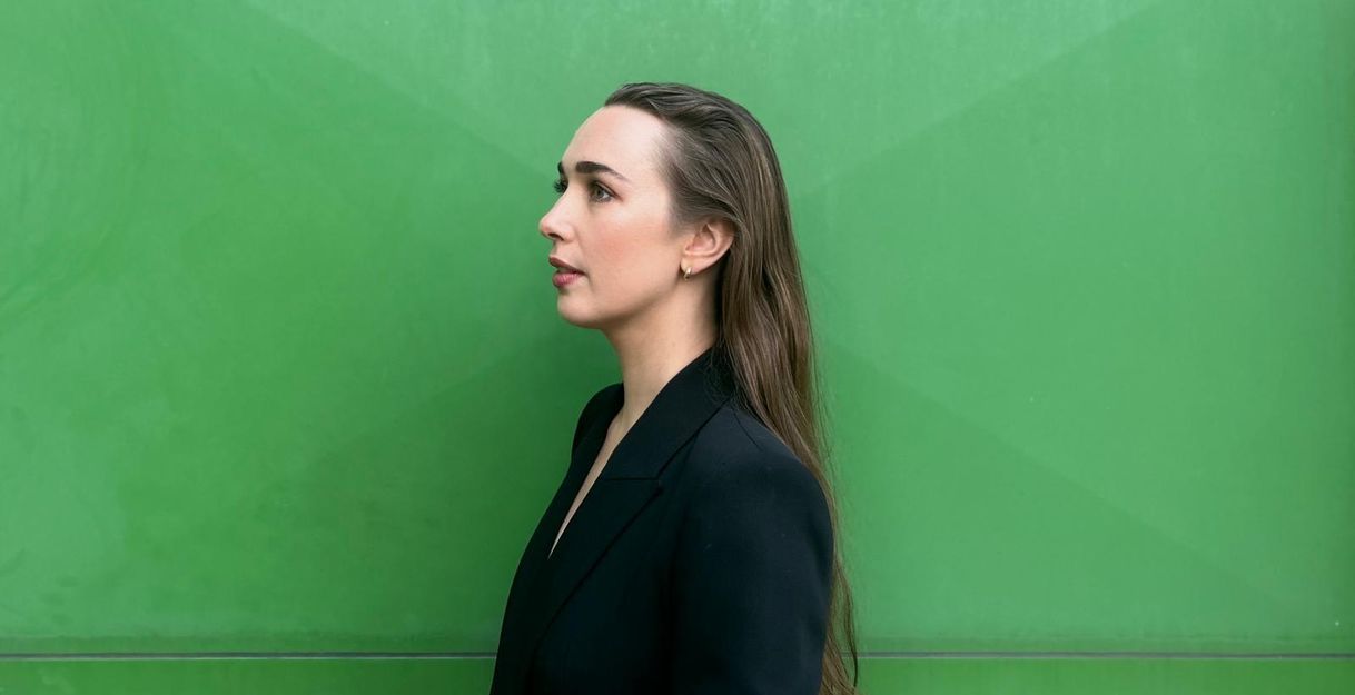 Die Sängerin Olivia Warburton steht vor einem grünen Hintergrund und sieht nach links.