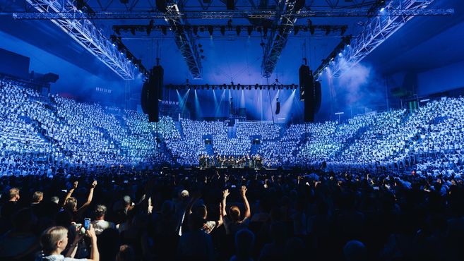 Großes Konzert mit Chor und Publikum in einer beleuchteten Arena.