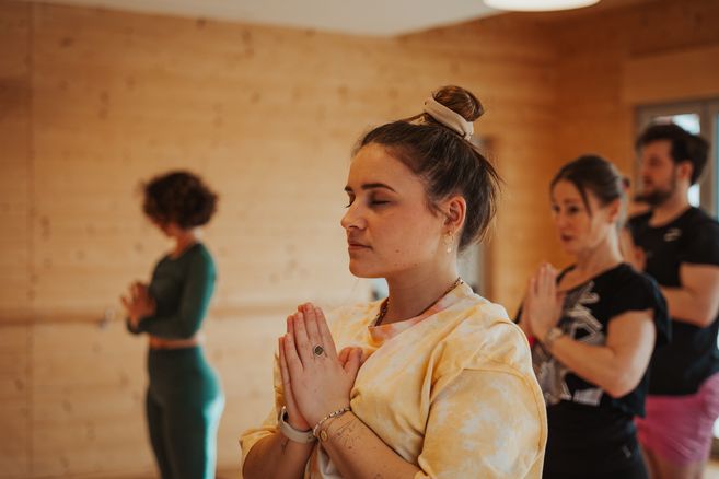 Menschen in einem Yoga-Kurs in einem Raum mit Holzwänden, die meditieren.