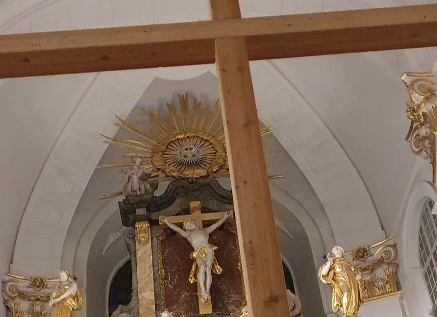 Innenansicht der St. Michaelis Kirche mit einem großen Holzkreuz im Vordergrund und einem kunstvollen Altar im Hintergrund.