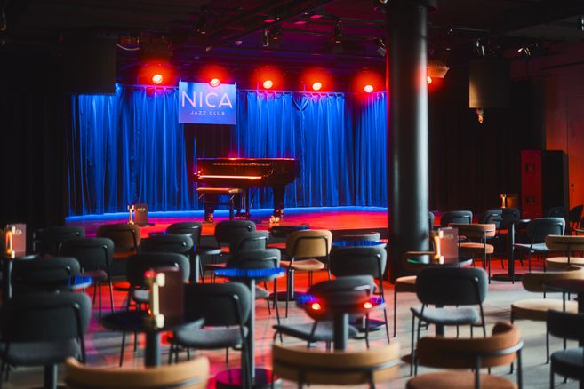 Innenansicht des NICA Jazz Clubs mit Bühne, Flügel und leeren Sitzplätzen.