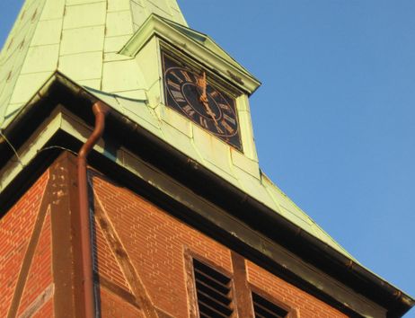 Nahaufnahme eines Kirchturms mit Uhr und grünem Dach vor blauem Himmel.